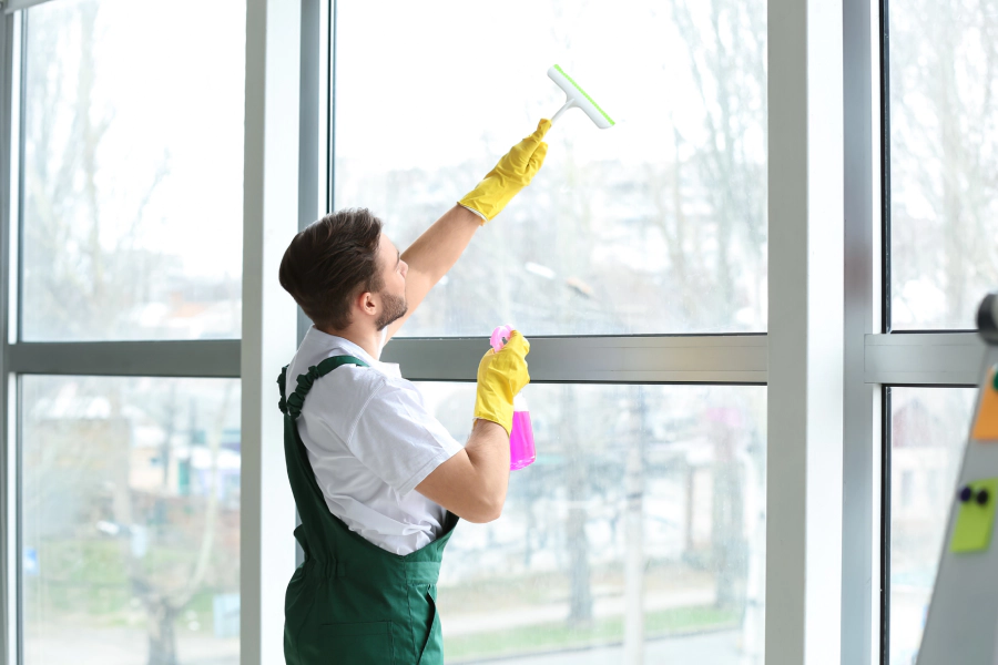 worker with a green jumpsuit and yellow gloves cleaning some glass windows
